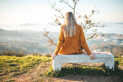 Rear view of woman sitting on bench against sky