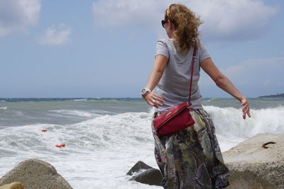 Woman standing on rock at beach against sky