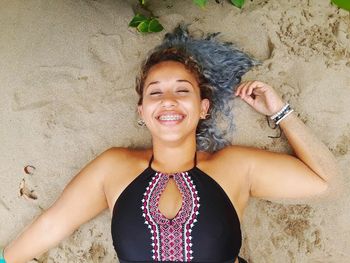 Portrait of smiling young woman lying on sand at beach