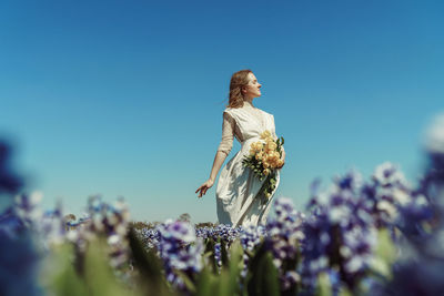 Woman standing by flowering plant against blue sky