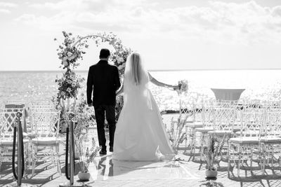 Rear view of bride and bridegroom standing by sea against sky