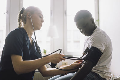 Female nurse checking blood pressure of male teenage patient sitting in clinic