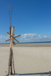 Wooden cross on sand at beach against sky