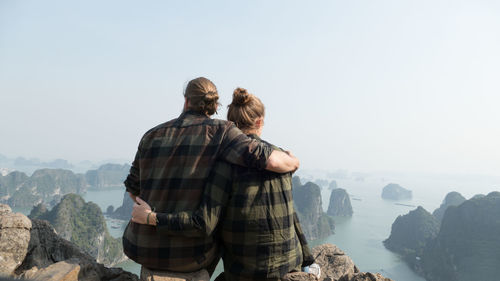 Rear view of couple sitting on rocks against sky