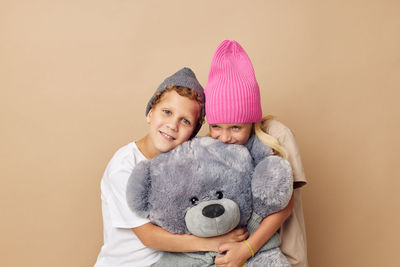 Cute sibling embracing stuffed toy against beige background