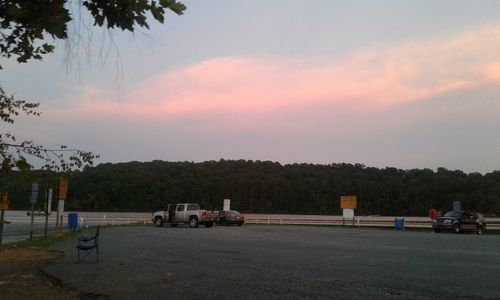 Cars on road by field against sky at sunset