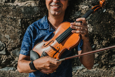 Midsection of man playing violin against wall