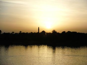 Scenic view of lake by silhouette trees against sky during sunset