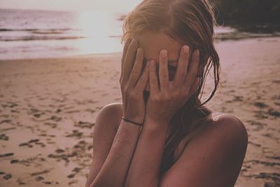 Young woman covering face with sand on beach