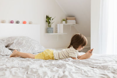 A little boy of four years lies on the bed and plays a mobile phone, a smartphone. children 