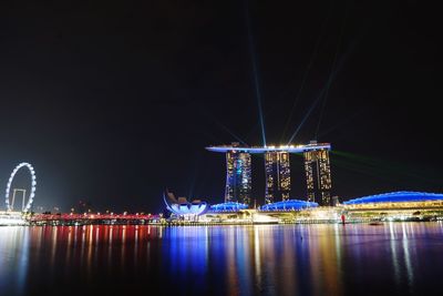 Illuminated marina bay sands by sea at night against clear sky