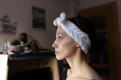 Side view of female with white headband deeply absorbed in thoughts sitting in dressing room and preparing for makeup