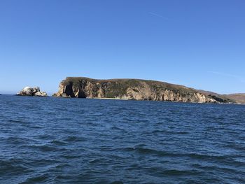 Rock formations in sea against clear blue sky