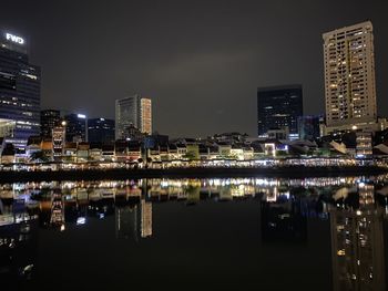 Illuminated buildings by river against sky at night