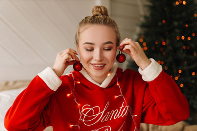 Smiling young woman holding baubles at earring at home