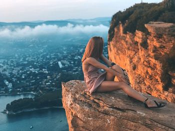 Rear view of woman sitting on rock against sea