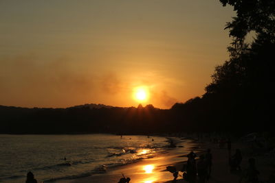 Silhouette people on shore against sky during sunset