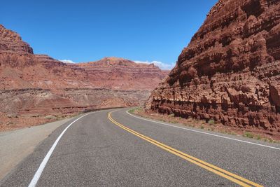 Road leading towards mountains against clear sky