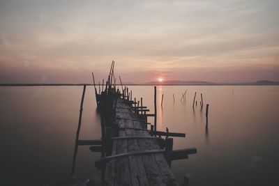 Sailboat on pier over sea against sky during sunset