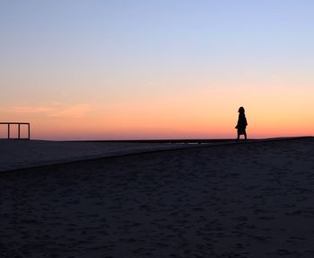 Silhouette man standing on beach against clear sky during sunset