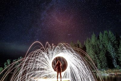 Rear view of woman with wire wool on pier over lake at night