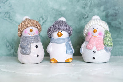 Three ceramic new year's toys, a penguin and snowmen in knitted hats and scarves.