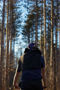 Rear view of man standing against trees in forest