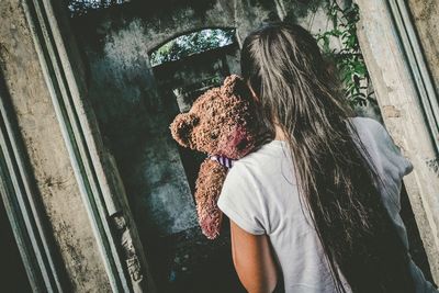 Rear view of woman with teddy bear standing on doorway