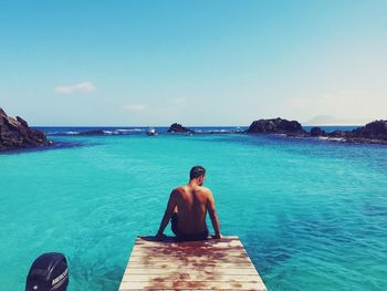 Full length of shirtless man sitting on sea against sky