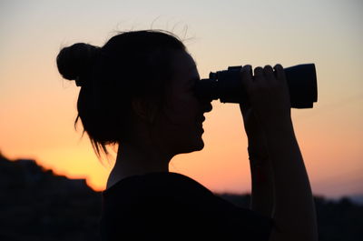 Silhouette woman photographing against sky during sunset