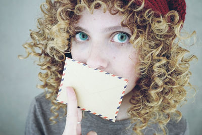 Portrait of serious young woman covering mouth with envelope against gray background