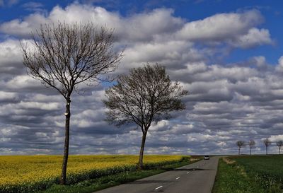 Road amidst field against cloudy sky