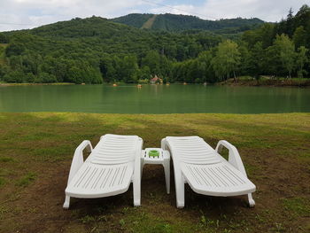 Deck chairs by lake against sky