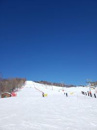 People skiing on snowcapped mountain against clear blue sky