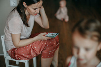 Mother in a home suit sits at home with two children and using mobile