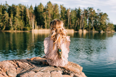 Young girl sat on a rock with feathers in her hair thinking