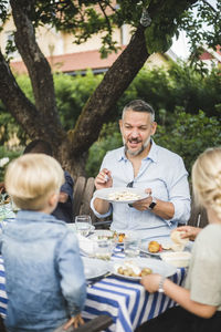 Mature man talking while showing food plate to children in party