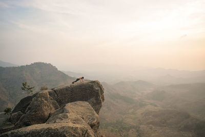 Young man standing on mountain against sky during sunset