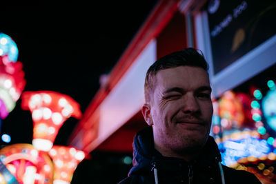 Low angle portrait of young man winking eye at amusement park