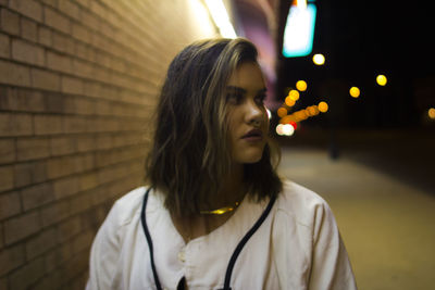 Close-up of young woman standing against illuminated wall at night