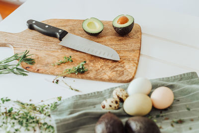 Cutting board with avocado, knife, thyme and rosemary and eggs