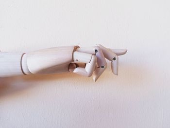 Close-up of hand holding stick on table against white wall