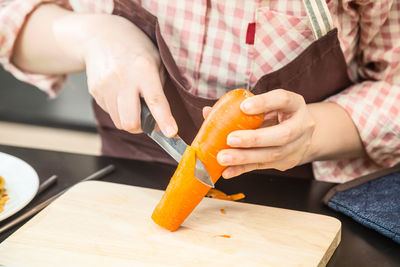 Midsection of woman cutting carrot on board