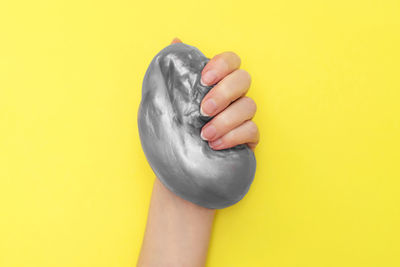 Close-up of human hand holding yellow leaf against gray background