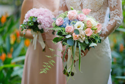 Bride holding bouquet while standing with bridesmaid during wedding ceremony