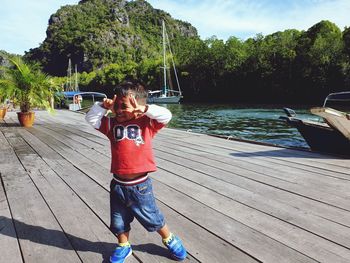 Full length of boy standing at harbor against mountains