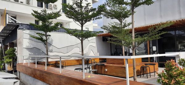 Empty chairs and tables by buildings against trees