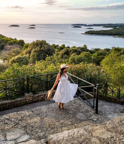 Woman standing on railing by sea against sky