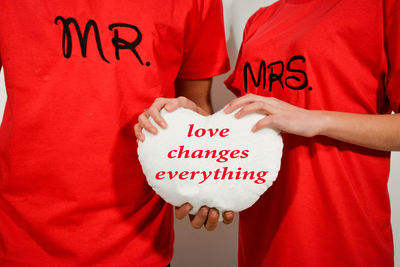 Midsection of couple holding heart shape with text