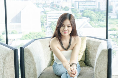 Smiling young woman looking away while sitting on chair against window